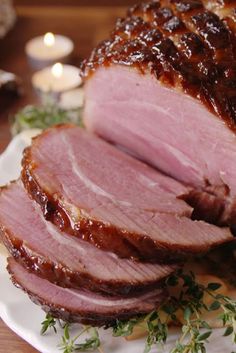 sliced ham sitting on top of a white plate next to some candles and sauces