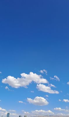 an airplane is flying high in the blue sky with clouds above it and buildings below