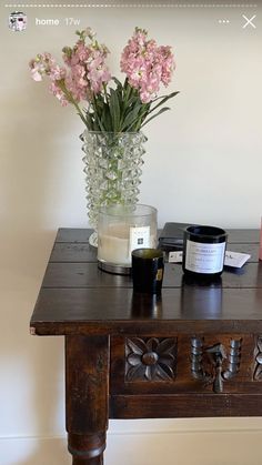 a wooden table topped with a vase filled with pink flowers and a candle on top of it