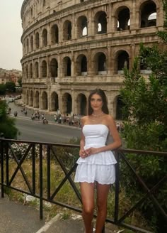 a beautiful young woman standing in front of an old roman colossion with her hands on her hips