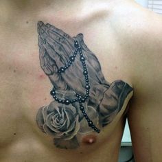 a man with a rosary and rose tattoo on his chest is holding a praying hand