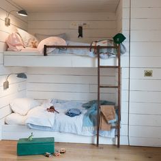 two bunk beds in a room with white walls and wood flooring, along with a green suitcase