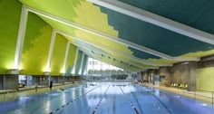 an indoor swimming pool with blue and green tiles on the ceiling, along with yellow lounge chairs