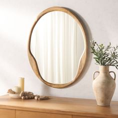 a round mirror sitting on top of a wooden dresser next to a vase and candle