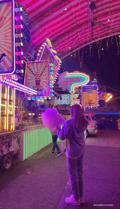 a girl standing in front of a carnival ride at night with lights on the ceiling