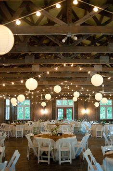 a room filled with lots of tables and chairs covered in white paper lanterns hanging from the ceiling