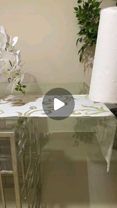 a glass table with white flowers on it and a roll of toilet paper next to it