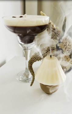 a glass filled with liquid sitting next to a candle on top of a white table