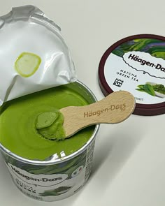 a can of green liquid with a wooden spoon in it next to a tin of haagen - dau