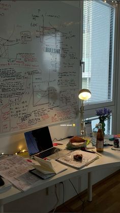 a laptop computer sitting on top of a white desk next to a window with writing all over it