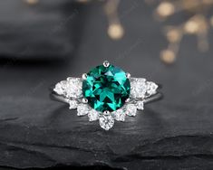 an emerald and diamond ring on top of a black rock