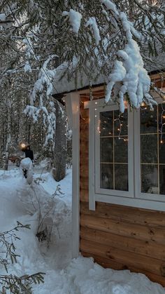 a small cabin in the woods with snow on the ground and lights hanging from the roof