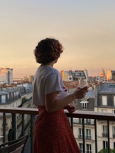 a woman standing on top of a balcony holding a glass of wine in her hand