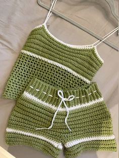 a crocheted green and white outfit hanging on a hanger next to a bed