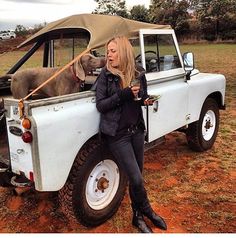 a woman sitting in the back of a pick up truck with a dog sticking its head out