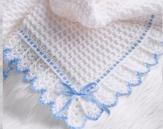 a crocheted baby blanket with blue trim on the edge and a white shirt underneath it