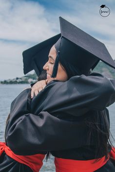 two graduates hugging each other in front of the water