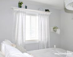 a white bed sitting next to a window in a room with curtains on the windowsill