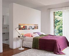 a bedroom with white walls and wooden floors, along with a large bed covered in purple blankets