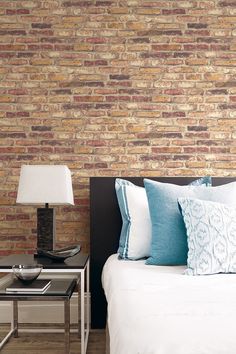 a bed sitting next to a lamp on top of a wooden table in front of a brick wall