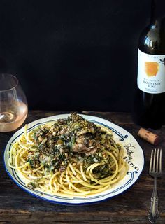 a plate of spaghetti with meat and spinach next to a bottle of wine on a wooden table