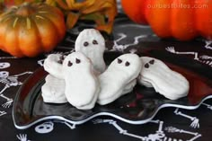 three ghost cookies sitting on top of a black plate next to pumpkins and other halloween decorations