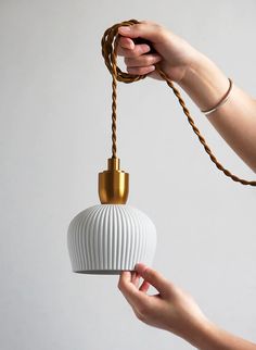 a hand holding a white and gold light fixture with a rope attached to the bulb