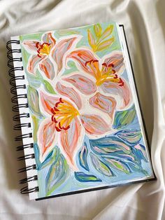 an art journal with flowers painted on the pages and colored pencils next to it