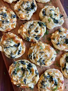 a wooden board topped with mini pizzas covered in cheese and spinach