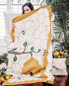 a woman holding up a yellow and white blanket in front of a window with potted plants