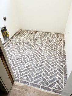 an empty room with white walls and grey flooring, next to a trash can