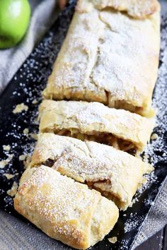 several pieces of apple turnover sitting on top of a black plate with powdered sugar