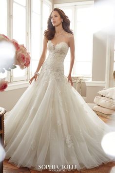 a beautiful woman in a wedding dress standing by a window