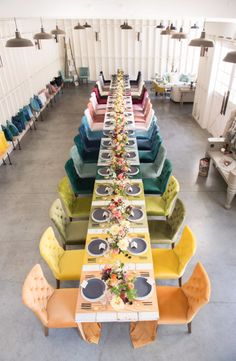 a long table is set up with colorful chairs and place settings for the dinner party