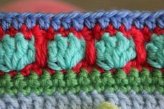 the crochet is colorfully colored and has green, blue, red, and white flowers on it