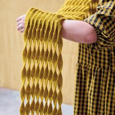 a woman is holding onto a yellow knitted scarf with wavy lines on the ends