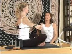 two women sitting on yoga mats in front of a tapestry