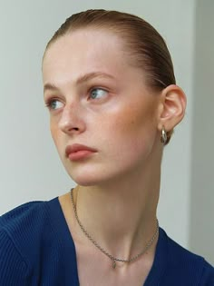 a woman wearing a blue sweater and silver necklace looking off into the distance with her eyes closed