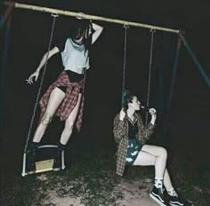 two people sitting on swings in the dark, one is holding onto another person's leg