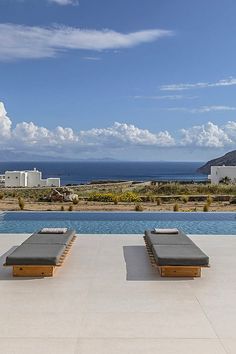 two lounge chairs sitting on top of a cement patio next to a swimming pool with the ocean in the background