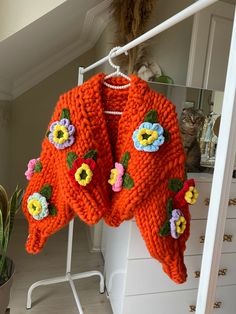 an orange sweater with flowers is hanging on a white rack in front of a cat