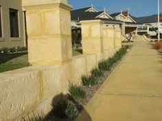 there is a sidewalk between two buildings with plants growing on the curb and grass in front of it