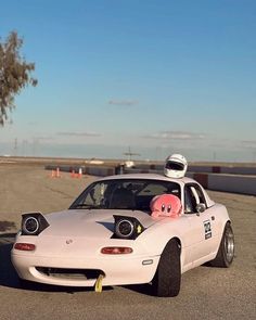 a white car with a pink stuffed animal in it's head driving down the road