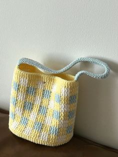 a crocheted yellow and blue purse sitting on top of a brown table next to a white wall