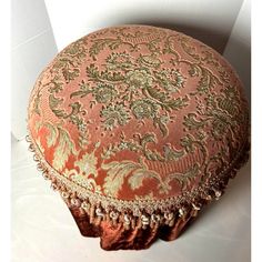 an orange and gold round ottoman with tassels on the bottom, sitting on a white surface