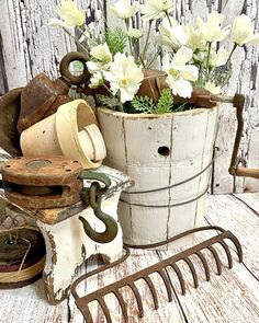 an old bucket with flowers in it sitting on a table next to a garden rake