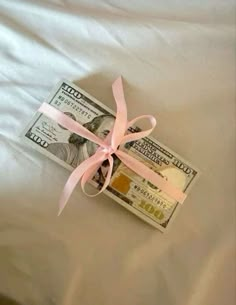 a bundle of money tied with a pink ribbon on top of a white bed sheet