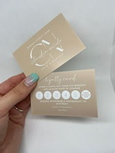 a person holding up two business cards on top of a white surface with gold foil