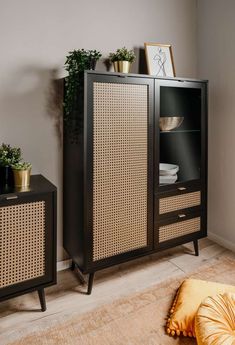 a black cabinet with wicker doors and drawers in a room next to a yellow pillow