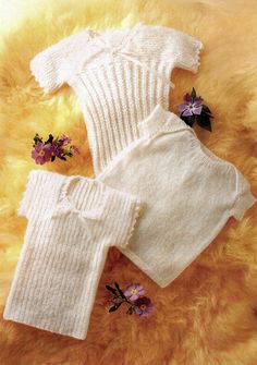 two white knitted sweaters and pants with flowers on the furnishing next to them